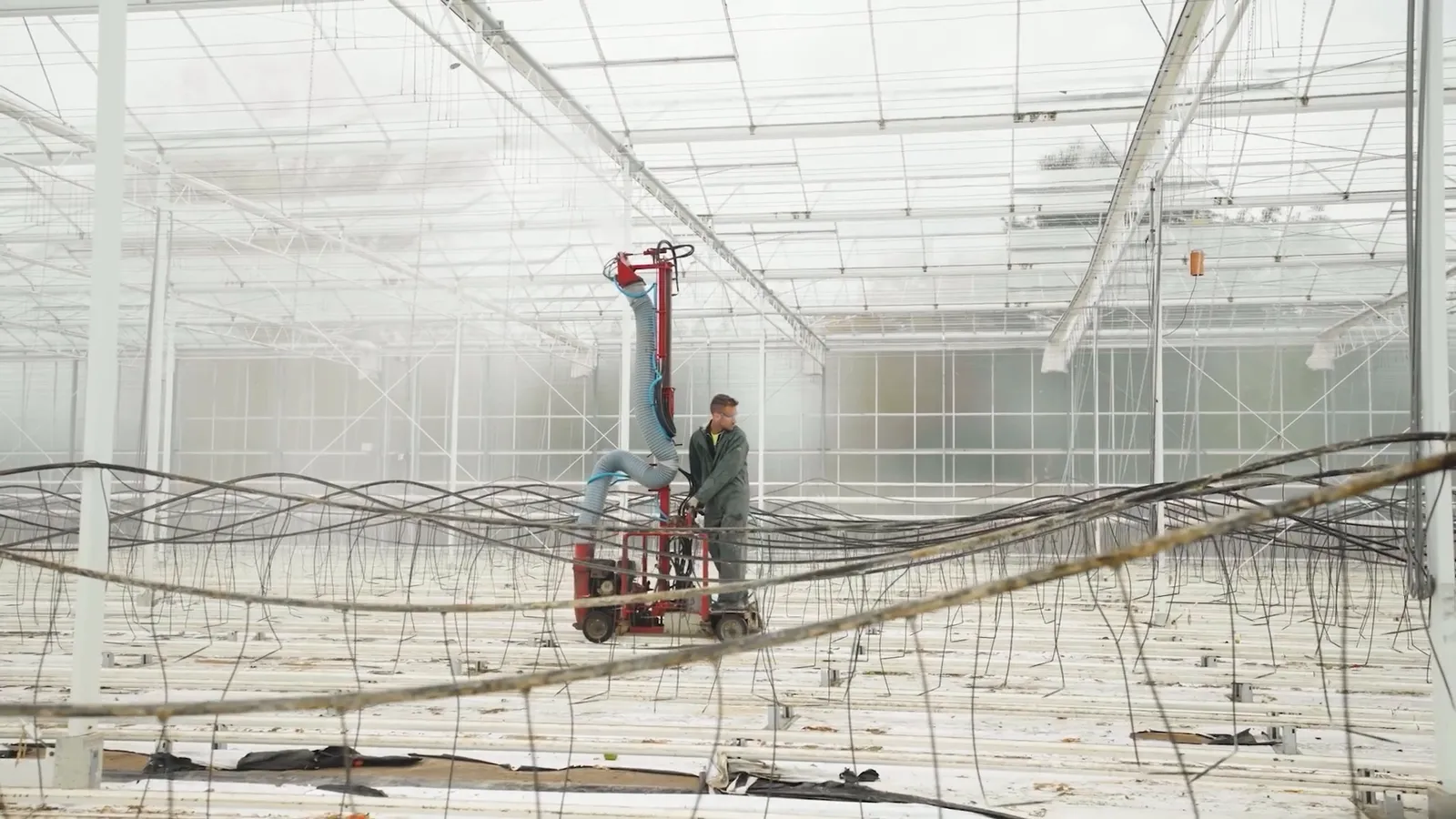 Beeld uit de headerfilm: de wasgiraf in de lege serre, de machinist op het platform naast de arm, met de teeltdraden op de voorgrond.